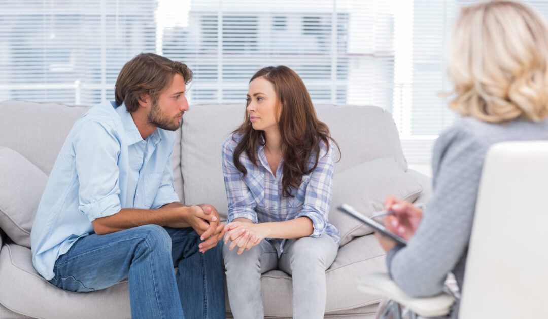 Couple looking to each other during therapy session while therapist watches