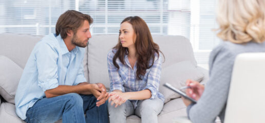 Couple looking to each other during therapy session while therapist watches